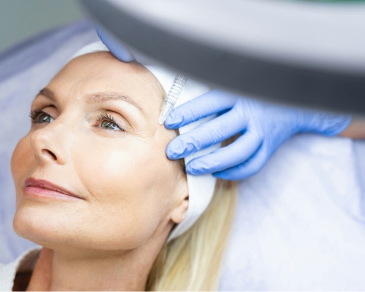 Middle-aged woman receiving a cosmetic facial injection from a gloved professional.